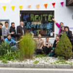 Eine Gruppe von Menschen steht vor der Auslage des Kostnixladens, der feierlich eröffnet wird.