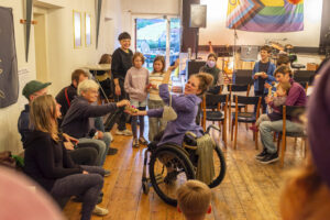Eine Gruppe von alten, jungen, kleinen, großen, Menschen mit und ohne Rollstuhl im Festsaal.