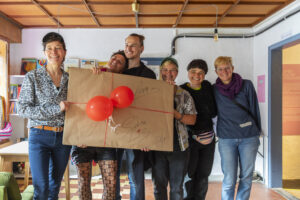 Übergabe eines Geschenks, das mit Unterschriften und Luftballons verziert ist.